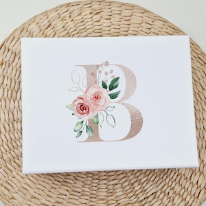 Puede incluir: Una impresi&oacute;n en lienzo blanco con una letra "B" de oro rosa decorada con flores de acuarela rosa y verde.