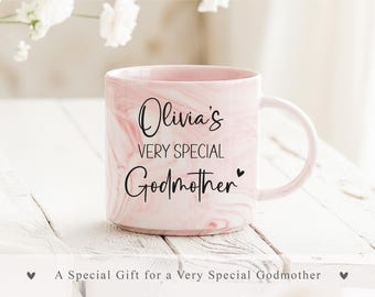 May include: A pink and white marbled ceramic mug featuring the black printed text Olivia's VERY SPECIAL Godmother with a small heart icon. The mug has a smooth finish, a rounded handle, and a cylindrical shape, presenting a clean and simple design.
