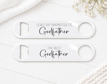 May include: Two white flat bottle openers with black text. The top opener reads LEVEL UP! PROMOTED TO Godfather. The bottom opener reads THE BEST Godfather. Each opener features a rectangular body with a circular hole on one end and a notch on the other.