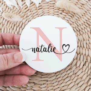 May include: A white round coaster with a pink letter N and the name "natalie" written in black cursive with a small heart next to it.