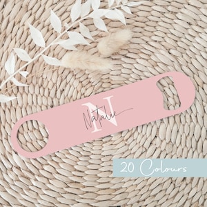 May include: A pink metal bottle opener with a white letter N and the name Natalie in black script. The bottle opener is on a woven surface.