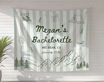 May include: A large, rectangular banner with a light green and white striped background. The banner features the text "Megan's Bachelorette" and the location and date. The design includes illustrations of mountains, trees, a compass, and a tent.
