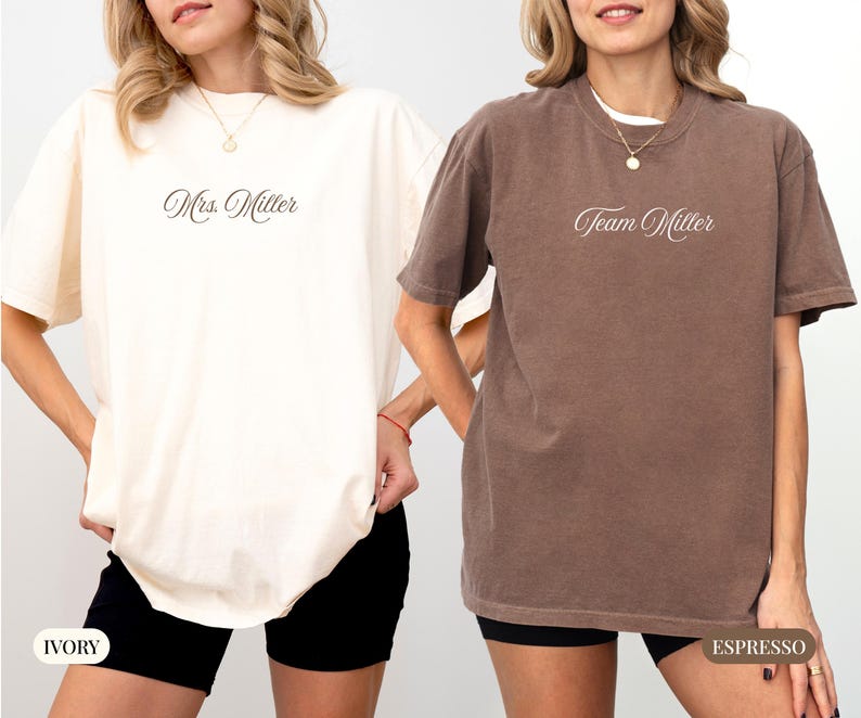 May include: Two short-sleeved t-shirts, one ivory and one espresso, with the text "Mrs. Miller" and "Team Miller" in cursive script. The shirts are worn with black shorts. The ivory shirt has a tag that says "IVORY" and the espresso shirt has a tag that says "ESPRESSO".