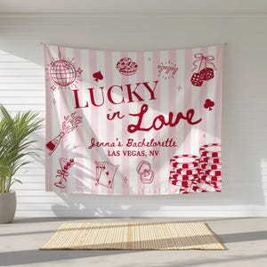 May include: A pink and white striped banner with red illustrations of casino-themed items, including dice, playing cards, and poker chips. The banner reads "Lucky in Love" and "Jenna's Bachelorette Las Vegas, NV."