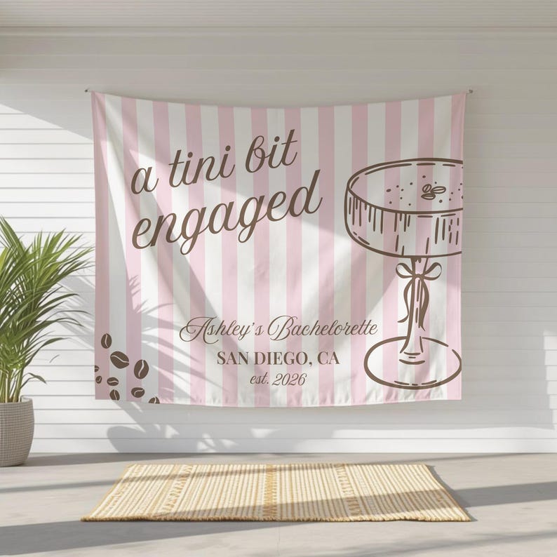 K&ouml;nnte beinhalten: Ein rosa-wei&szlig; gestreifter Banner mit dem Text "a tini bit engaged" in brauner Schrift. Das Banner zeigt auch eine braune Illustration eines Kuchens und den Text "Ashley's Bachelorette, San Diego, CA, est. 2026".