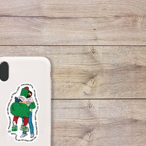 May include: A white phone case with a sticker of two people hugging a green cactus. The sticker has the text "Philadelphia - No one likes us, we don't care - Philadelphia - No one likes us, we don't care" around the image.