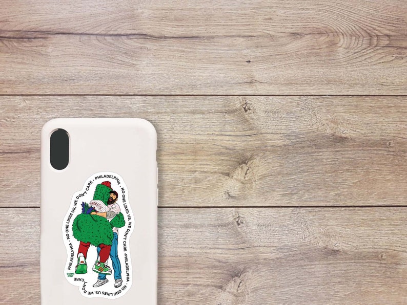 May include: A white phone case with a sticker of two people hugging a green cactus. The sticker has the text "Philadelphia - No one likes us, we don't care - Philadelphia - No one likes us, we don't care" around the image.