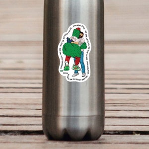 May include: A white sticker with a green, cartoon cactus hugging a person. The sticker has text that reads "NO ONE LIKES US WE DON'T CARE" PHILADELPHIA, NO ONE LIKES US WE DON'T CARE" PHILADELPHIA.