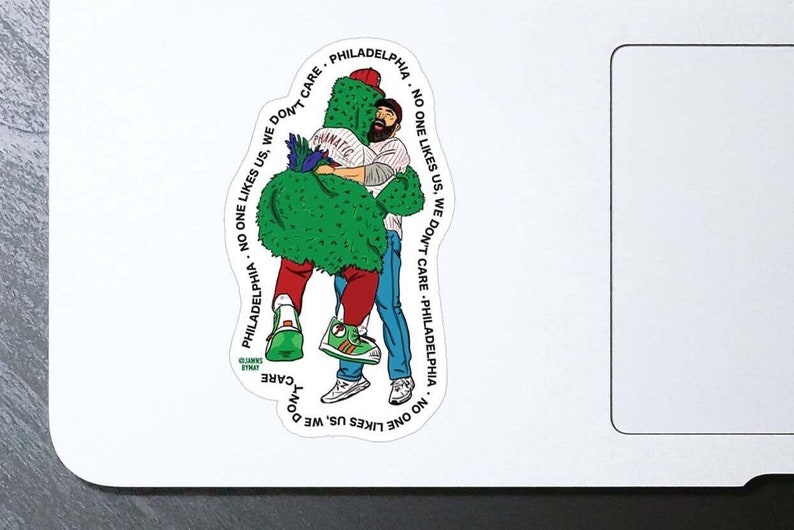 May include: A green and white mascot character with a man in a red and blue baseball uniform hugging it. The text around the image reads "Philadelphia - No one likes us, we don't care - Philadelphia - No one likes us, we don't care - Philadelphia".