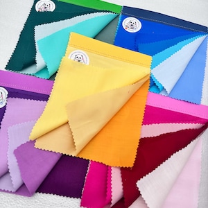 May include: A collection of fabric swatches in various colors, including teal, yellow, orange, pink, and purple. Each swatch has a contrasting color on the underside and a small sticker with a panda logo. The edges are serged.
