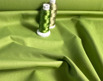 May include: Two spools of thread, one green and one beige, on a green fabric background.