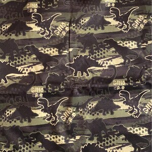 May include: A black and green fabric with a repeating pattern of dinosaurs. The dinosaurs are in a variety of poses, including walking, running, and roaring. The fabric has a camouflage pattern with brown, green, and black colors.