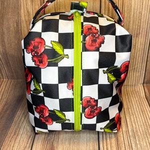 May include: A black and white checkered zippered pouch with a skull and cherry design. The pouch has a green zipper and a black handle.