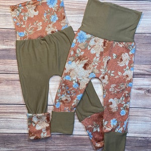May include: Two pairs of olive green and brown floral print leggings with a high waist and cuffed ankles.