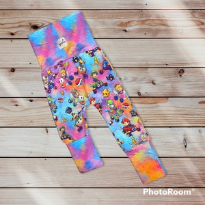 May include: A pair of colorful baby leggings with a tie-dye pattern and a print of various video game characters. The leggings are made of soft, comfortable fabric and are perfect for everyday wear.