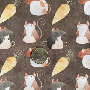 May include: A brown fabric with a repeating pattern of white, brown, and black mice holding carrots. The fabric has a subtle texture and a vintage aesthetic.