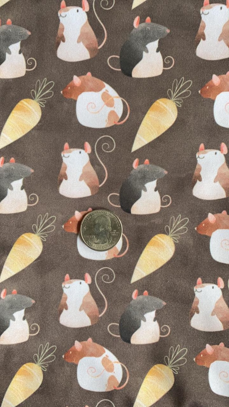 May include: A brown fabric with a repeating pattern of white, brown, and black mice holding carrots. The fabric has a subtle texture and a vintage aesthetic.