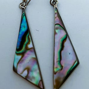 May include: A pair of silver-tone earrings with a triangular shape. The earrings feature iridescent abalone shell in shades of blue, green, pink, and brown. The earrings have a hook closure.