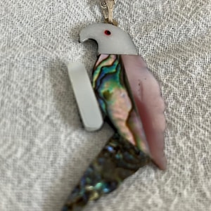May include: A silver chain necklace with a pink, green, and blue abalone shell parrot pendant.