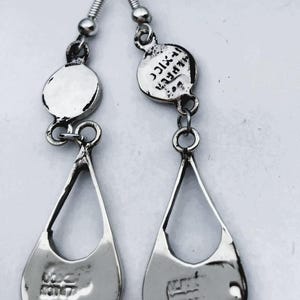 Puede incluir: Un par de pendientes colgantes plateados. Cada pendiente presenta un colgante en forma de l&aacute;grima con un dise&ntilde;o estampado y una pieza superior circular. Los pendientes est&aacute;n conectados por peque&ntilde;os anillos y un gancho.