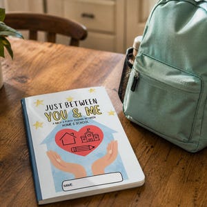 May include: A journal titled "Just Between You & Me" with a blue cover and a heart-shaped graphic featuring a house, school, and pencil. A teal backpack sits nearby on a wooden table. The journal is designed for home and school communication.