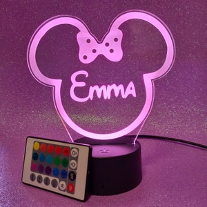 May include: A pink and white night light shaped like a cartoon mouse head with a bow. The light has a remote control with multiple color options and the name "Emma" is written on the front.
