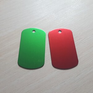 Puede incluir: Dos etiquetas de perro de metal en blanco, una verde y una roja.