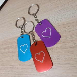 Puede incluir: Tres llaveros con dise&ntilde;os en forma de coraz&oacute;n. Los llaveros est&aacute;n unidos a anillos plateados y tienen una cadena plateada. Los llaveros son azules, morados y rojos.