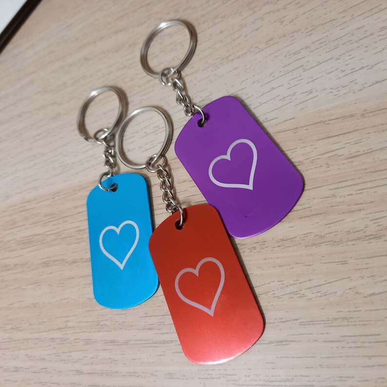 Puede incluir: Tres llaveros con dise&ntilde;os en forma de coraz&oacute;n. Los llaveros est&aacute;n unidos a anillos plateados y tienen una cadena plateada. Los llaveros son azules, morados y rojos.