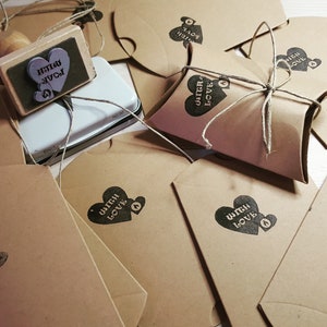 Puede incluir: Una colecci&oacute;n de bolsas de papel marr&oacute;n con un coraz&oacute;n y el texto "Witch Love" estampado en ellas. Las bolsas est&aacute;n atadas con cuerda y algunas est&aacute;n dobladas en forma de almohada. Tambi&eacute;n se ve un sello de madera con el texto "Witch Love".