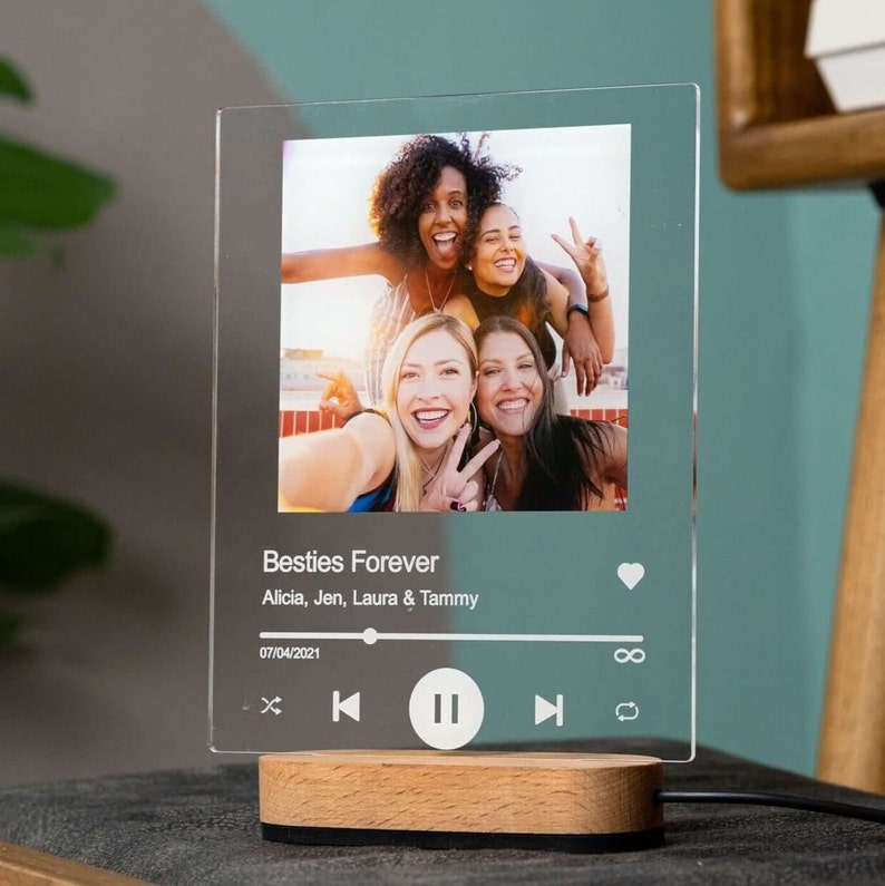 May include: A clear glass photo frame with a picture of four friends smiling. The frame has a music player design with a play button, a heart icon, and the text "Besties Forever Alicia, Jen, Laura & Tammy 07/04/2021".