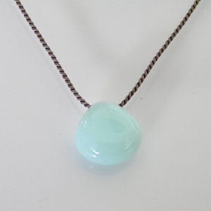 May include: A light blue gemstone pendant on a brown cord necklace.
