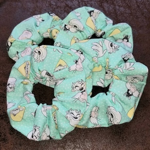 May include: Three green scrunchies with a white polka dot pattern and a cartoon print of a cat and mouse.