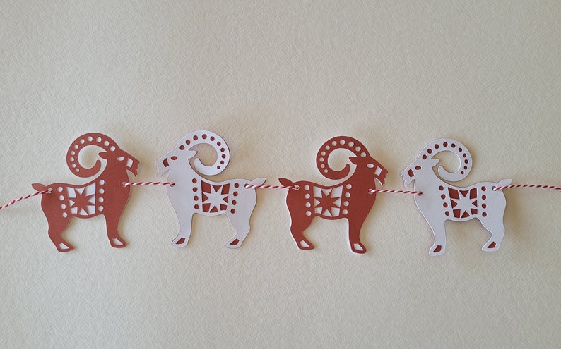 May include: A string of paper cutouts of red and white goats with intricate designs. The goats are connected by a red and white string.