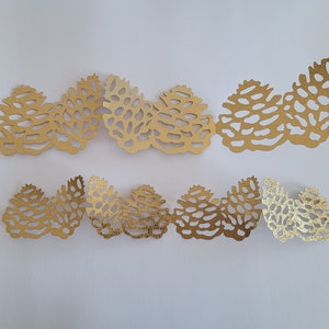 May include: Gold paper cutouts of pine cones in a repeating pattern. The pine cones are arranged in a wave-like pattern.