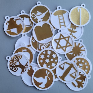 May include: A collection of 17 round, white paper ornaments with gold foil accents. Each ornament features a different symbol, including a dove, a star of David, a ladder, a tree, a scale, a lamp, a book, a star, a peace sign, and a hand holding a staff.