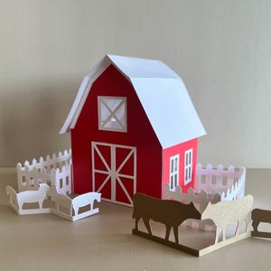 Peut inclure: Une scène de ferme en papier avec une grange rouge et un toit blanc, une clôture blanche et des animaux en papier découpé. La grange a une porte blanche et des détails de fenêtres. La scène comprend des moutons et des vaches en papier découpé.