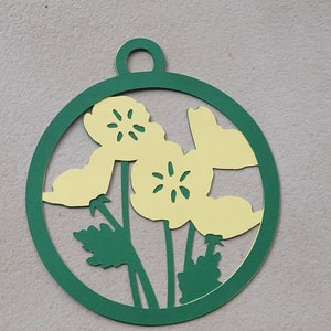 May include: A green paper circle ornament with a cut-out design of yellow flowers and green leaves.