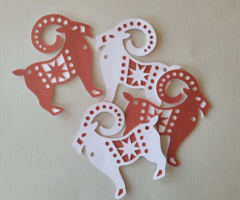 May include: Four paper cutouts of stylized rams with geometric patterns. The rams are in shades of red and white.