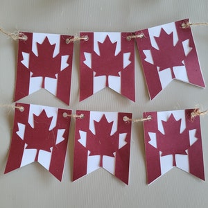 May include: A red and white Canadian flag banner with maple leaf cutouts. The banner is strung together with twine.