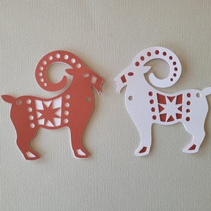 May include: Two paper cutouts of goats, one red and one white, with a star design. The goats are facing opposite directions.