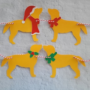 May include: A Christmas garland with four yellow paper cutouts of dogs wearing festive accessories. The dogs are connected by red and white string. One dog wears a Santa hat, another wears a red bow, and the other two wear green holly wreaths.