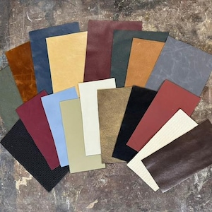 May include: A collection of rectangular leather swatches arranged in a fan pattern, featuring a diverse palette of colors including black, brown, tan, cream, navy, olive green, burgundy, light blue, grey, and red with various smooth and textured finishes.