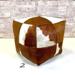 May include: A square brown and white cowhide ottoman with a patchwork design.