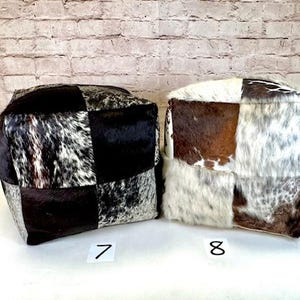 May include: Two square patchwork cowhide ottomans in black, brown, and white. The ottoman on the left is labeled "7" and the ottoman on the right is labeled "8".