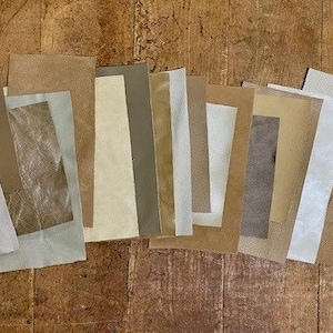 May include: A collection of 13 fabric swatches in various shades of brown, beige, and white. The swatches are arranged in a row on a wooden surface.