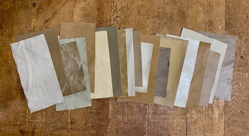 May include: A collection of 13 fabric swatches in various shades of brown, beige, and white. The swatches are arranged in a row on a wooden surface.