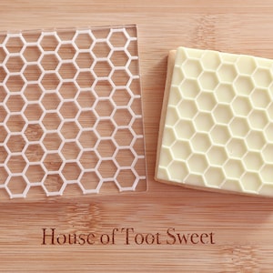 May include: A clear acrylic stamp with a honeycomb pattern and a square biscuit with a honeycomb design. The stamp has the text "HOTS" on the side. The biscuit is light yellow. The text "House of Toot Sweet" is at the bottom.