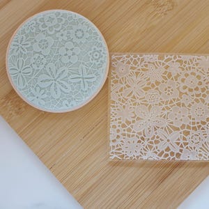 May include: A round, pale blue cookie stamp and a square, clear acrylic stamp, both with a detailed floral lace design. These stamps are intended for baking and crafts, adding an elegant touch to biscuits, fondant, or other creative endeavours.
