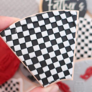 May include: A wedge-shaped cookie with a black and white chequered pattern. The cookie's design features a detailed arrangement of alternating black and white squares. Other cookies with different designs are visible.